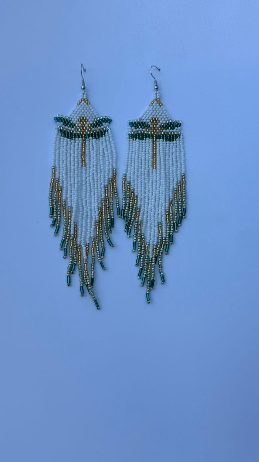 Long rectangular drop earrings with white pearl seed bead panel featuring a teal and gold diamond geometric motif, white and gold metallic fringe with teal bugle bead tips, silver fish-hook closures.
