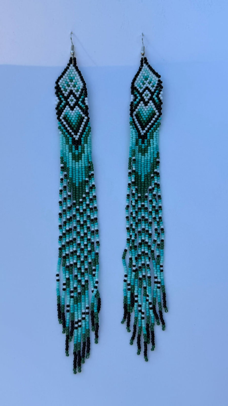Very long fringe drop earrings with nested diamond chevron header panel in black, white, aqua, and hunter green seed beads, extra-long fringe continuing the chevron colour pattern the full length, silver fish-hook closures.