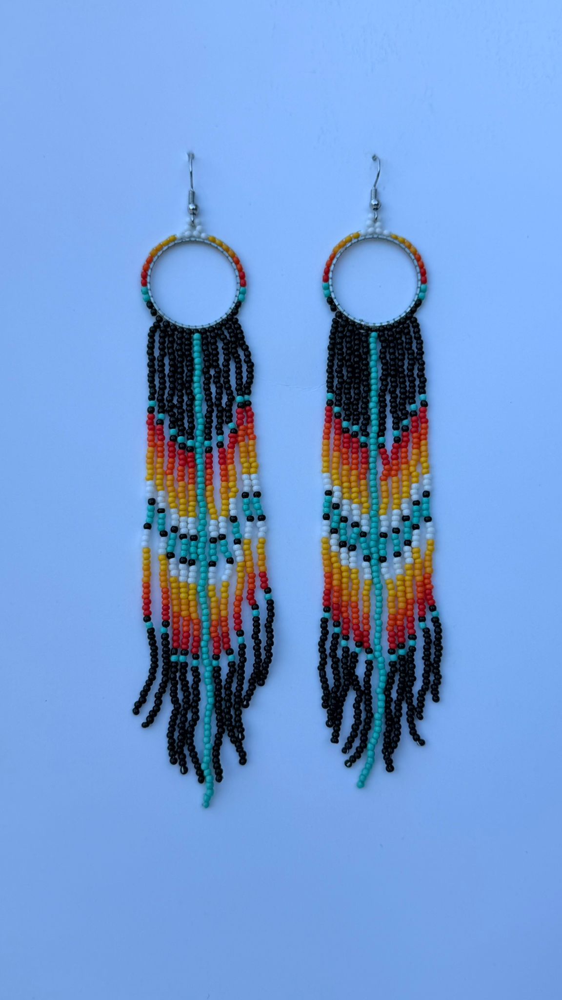 Pair of beaded drop earrings with white, teal, red, and yellow strands on triangular hoops.