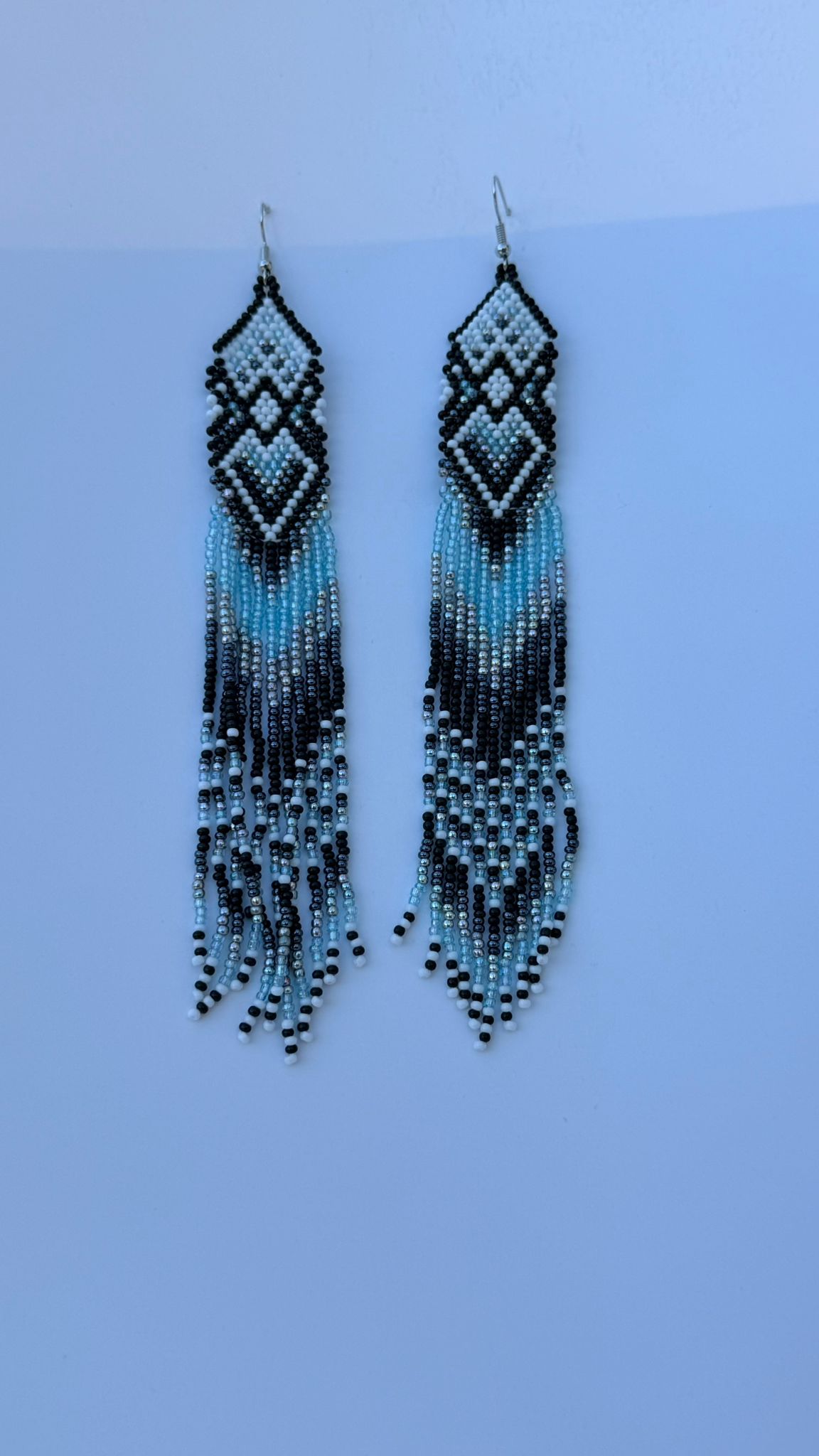 Teal geometric beaded earrings with black and white accents and fringed strands.