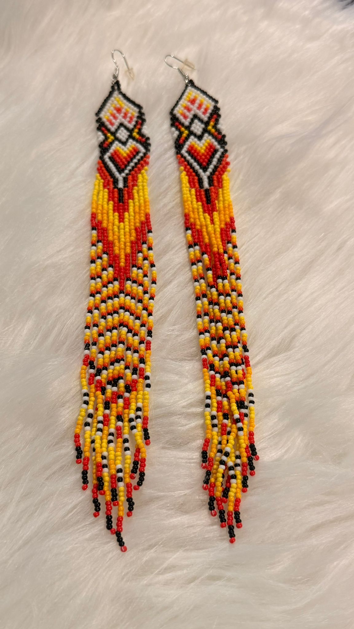 Long beaded earrings with geometric tops and red-orange fringes.